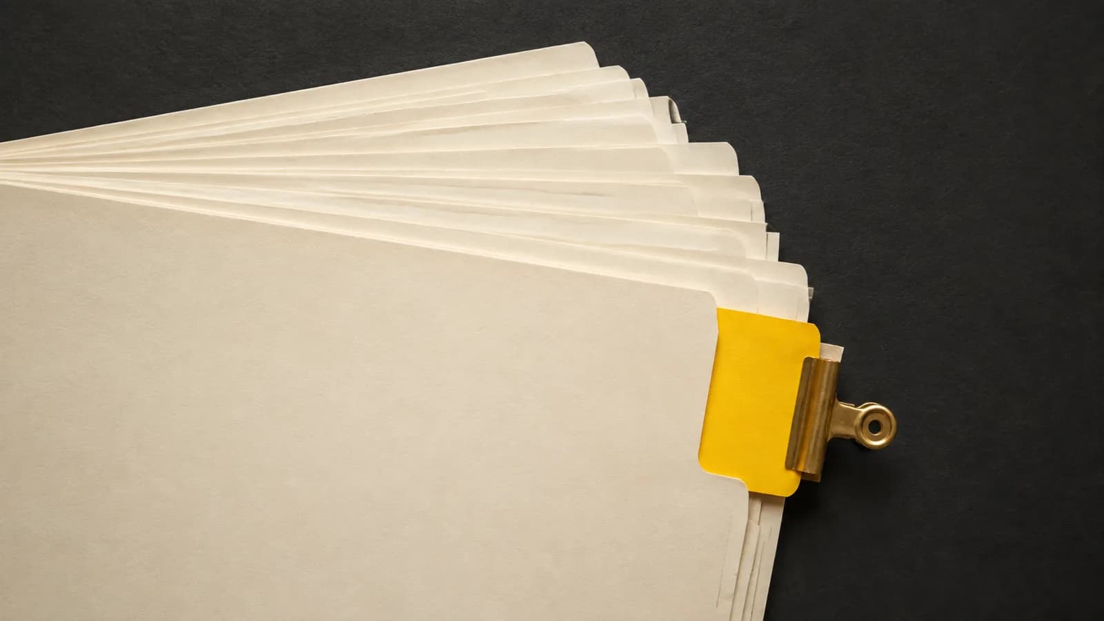 A carefully ordered fan of blank ivory document sleeves with one mustard-yellow tab held outside the stack by a brass clip. Conceptual editorial illustration.